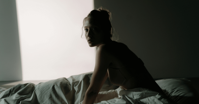 Woman in bed staring at the camera in a dark room.