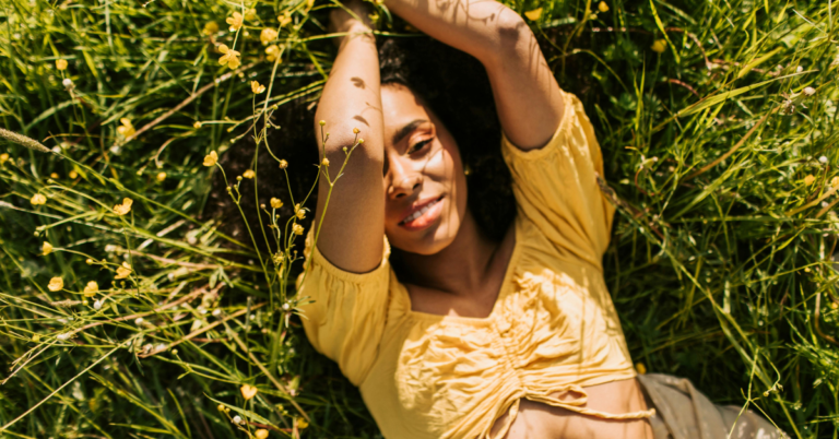 Woman laying in the grass and smiling up at the sun