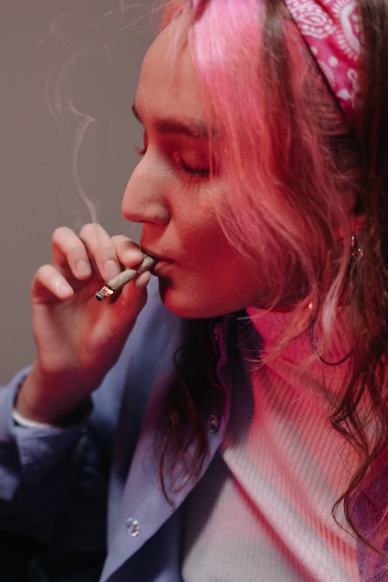 A young woman with pink hair smokes indoors, creating a relaxed and alternative atmosphere.