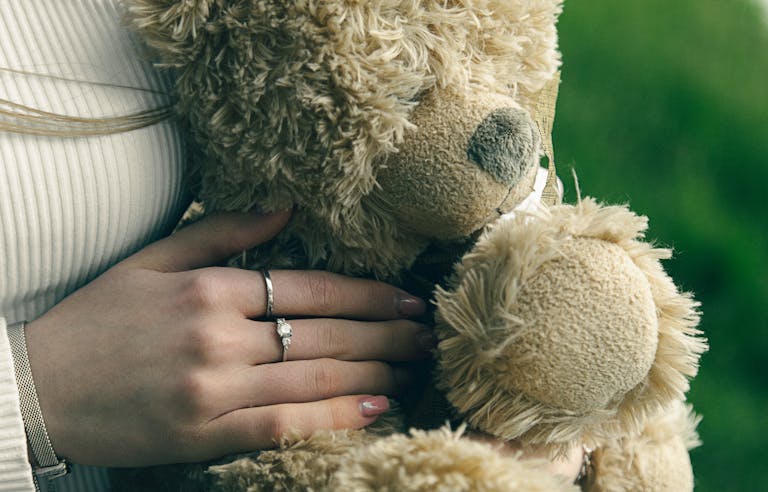 Hands embracing a plush teddy bear outdoors, showcasing comfort and warmth.