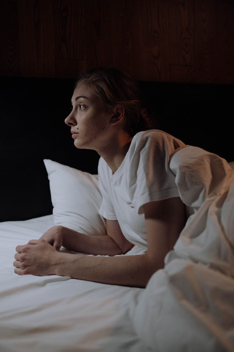 A woman lying in bed, deep in thought, illuminated by soft lighting at night.